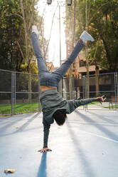 Akrobatischer Mann mit Hupenschild macht Handstand auf dem Basketballplatz auf dem Campus im Herbst - JMPF00792