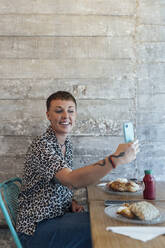 Lächelnde Frau, die ein Selfie mit ihrem Mobiltelefon macht, während sie im Restaurant sitzt - JRVF00104