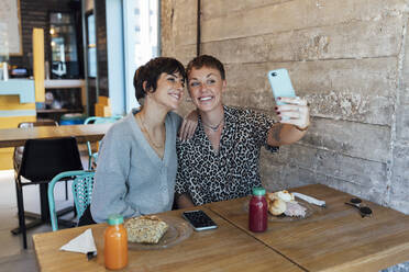 Young friends smiling while taking selfie through mobile phone sitting at restaurant - JRVF00106