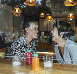 Glückliche Freunde, die lachend am Fenster des Restaurants sitzen - JRVF00108