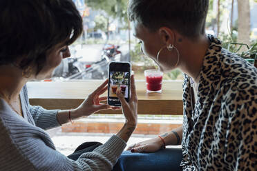 Junge Frau fotografiert ein Getränk mit dem Handy, während sie mit einem Freund im Restaurant sitzt - JRVF00111