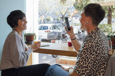 Frau, die einen lächelnden Freund mit dem Handy fotografiert, während sie im Restaurant sitzt - JRVF00112