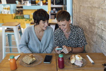 Woman using mobile phone while sitting by friend at restaurant - JRVF00117