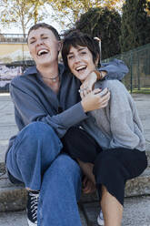 Cheerful woman embracing friend while sitting on steps - JRVF00139