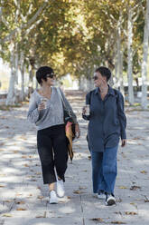 Junge Frauen mit Kaffeetasse im Gespräch auf dem Fußweg - JRVF00143