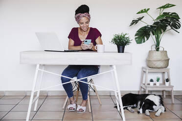 Lächelnde Unternehmerin, die ihr Smartphone an einer weißen Wand im Büro zu Hause benutzt - EBBF02207