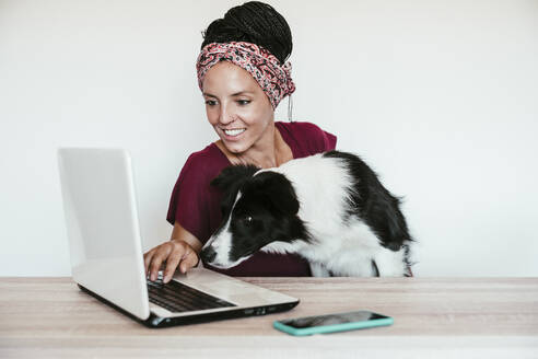 Freiberuflerin mit Border Collie benutzt Laptop auf dem Tisch im Büro zu Hause - EBBF02220