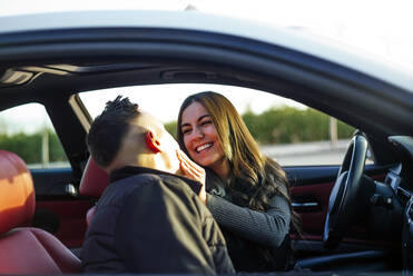 Girlfriend smiling while looking at boyfriend sitting in car - OCMF01977