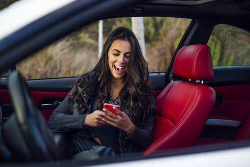 Excited woman using mobile phone while sitting in car - OCMF01992