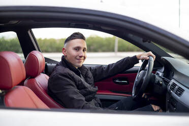 Junger Mann lächelt, während er im Auto sitzt - OCMF01996