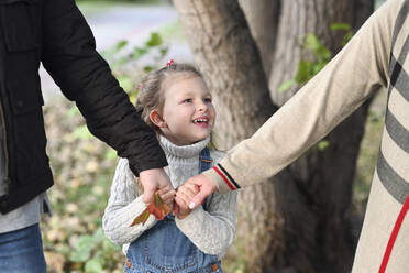 Lächelndes Mädchen hält Mutter und Vater im Park an der Hand - EYAF01457