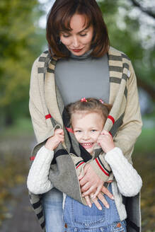 Glückliches Mädchen versteckt sich in Mutters Strickjacke im Park - EYAF01458