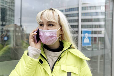 Close-up of young woman wearing face mask talking over mobile phone in city - FLLF00571