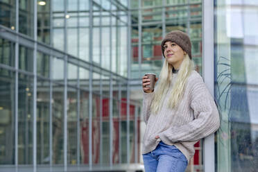 Junge Frau mit Kaffee vor einem modernen Gebäude in der Stadt - FLLF00575