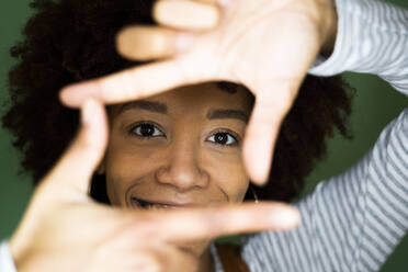 Afro junge Frau schaut durch Fingerrahmen - GIOF10695