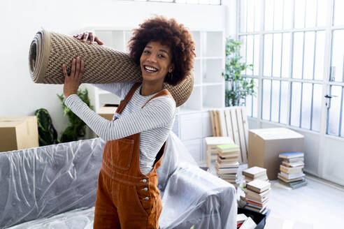 Glückliche Afro-Frau trägt Teppich beim Umzug in ein neues Haus - GIOF10718