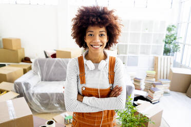 Happy young woman with arms crossed standing in new loft apartment - GIOF10739
