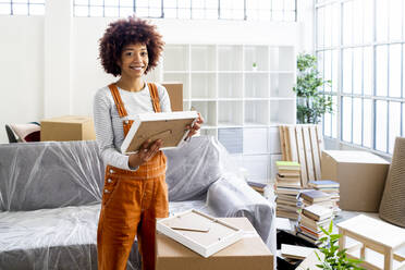 Happy Afro woman holding picture frame while moving into new loft apartment - GIOF10745