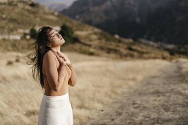 Junge Frau mit geschlossenen Augen in einem Feld bei Sonnenuntergang stehend - TCEF01429