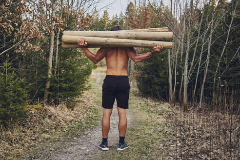 Männlicher Athlet ohne Hemd trägt Baumstämme im Wald - KDF00741