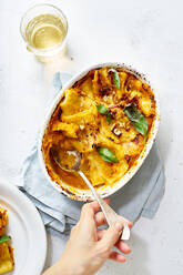 Top view of crop anonymous female with spoon taking tasty homemade squash served on table in baking dish - ADSF20188