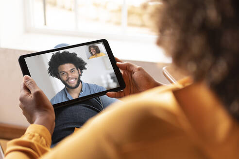 Frau im Gespräch mit lächelnden Mann auf Video-Anruf durch digitale Tablet beim Sitzen zu Hause - SBOF02451
