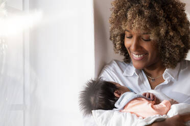 Smiling woman holding newborn baby while standing at home - SBOF02452