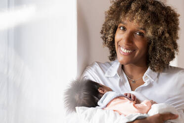 Happy woman holding newborn baby while standing at home - SBOF02454