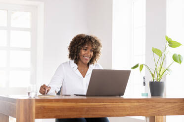 Lächelnde Geschäftsfrau, die im Büro zu Hause am Laptop arbeitet - SBOF02489