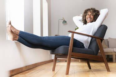 Happy woman smiling while resting on armchair at home - SBOF02511