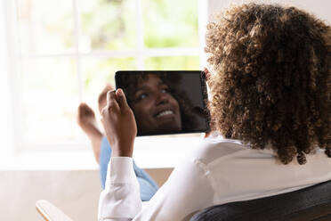 Lächelnde Frau mit digitalem Tablet, die wegschaut, während sie zu Hause sitzt - SBOF02513