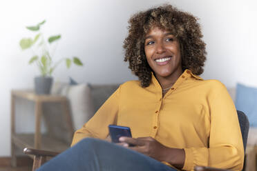 Mid adult woman with mobile phone looking away while sitting at home - SBOF02536