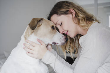 Nahaufnahme einer Frau mit geschlossenen Augen, die ihren Hund zu Hause liebt - EBBF02267