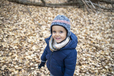 Cute boy wearing warm clothing standing on autumn leaves in forest - IFRF00328