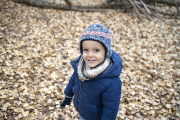 Niedlicher Junge in warmer Kleidung steht auf Herbstblättern im Wald - IFRF00328
