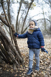 Cute boy wearing warm clothing looking away while standing in forest during autumn - IFRF00330