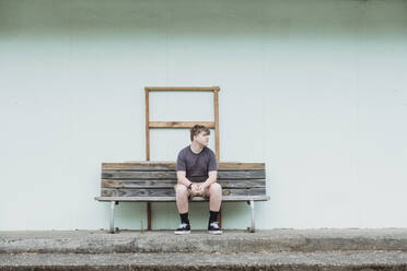 Jugendlicher, der allein auf einer Holzbank sitzt - CAVF91917