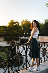 Beautiful woman standing by railing against clear sky in park during sunset - JMPF00821