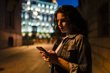 Beautiful woman looking away while using mobile phone in city at dusk - JMPF00840