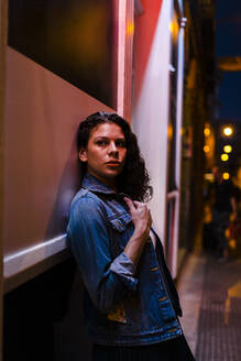 Thoughtful young woman leaning on wall in city at night - JMPF00841