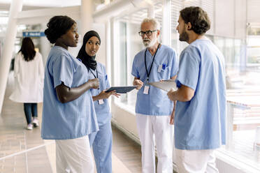 Confident male and female nurses talking in hospital corridor - MASF21244