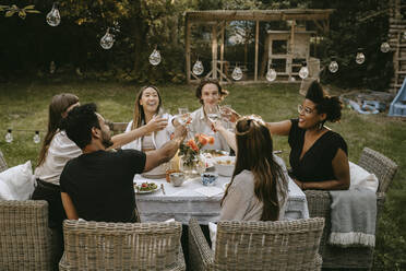 Smiling male and female friends toasting drinks while enjoying during social gathering - MASF21260