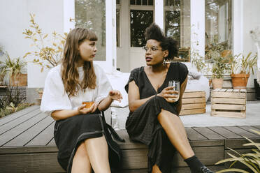 Female with drinking glass talking to friend while sitting in yard - MASF21278