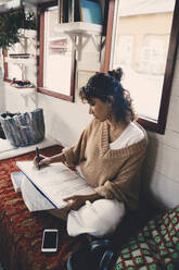 Mittlere erwachsene Frau zeichnet Skizze in Buch auf Hausboot - MASF21310