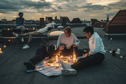 Männliche und weibliche Freunde unterhalten sich bei Sonnenuntergang auf der Terrasse eines Gebäudes - MASF21355