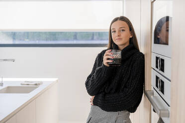 Teenage girl with drink standing by appliance in kitchen - DLTSF01527