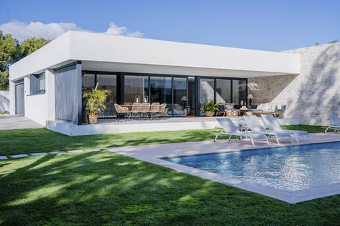 Empty lounge chairs at poolside against modern house - DLTSF01532