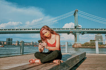 Young woman by river wearing face mask with phone. - CAVF91927