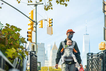 Vater trägt seine süße Tochter in der Babytrage beim Spaziergang in der Stadt während COVID-19 - CAVF91947