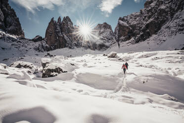 Zwei Alpinisten beim Abstieg auf verschneitem Weg gegen die Sonnenstrahlen in den Dolomiten - CAVF91968